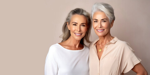 Portrait of two chic beautiful gray-haired mature women 50-60 years old in elegant clothes on gray background. Elderly woman smiles and looks at camera. Beautiful old age, cosmetology, face lifting