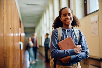 Happy black teenage girl in high school hallway looking at camera.