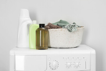 Baby clothes in wicker basket and laundry detergents on washing machine near light wall