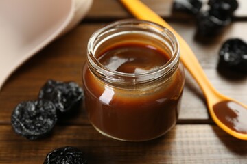 Tasty baby food in jar, spoon and dried prunes on wooden table, closeup