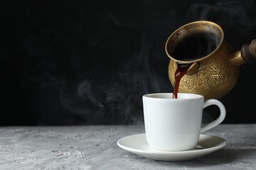 Turkish coffee. Pouring brewed beverage from cezve into cup at grey table. Space for text