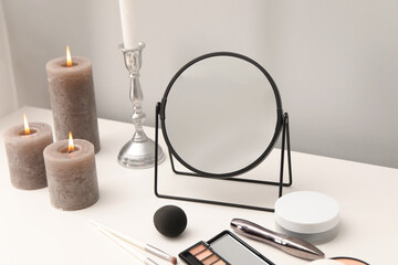 Dressing table with mirror, cosmetic products and burning candles in makeup room