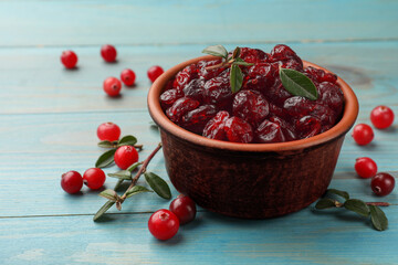 Tasty dried cranberries in bowl, fresh ones and leaves on light blue wooden table, closeup