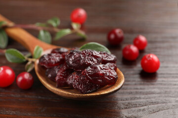 Tasty dried cranberries in spoon and fresh ones on wooden table, closeup