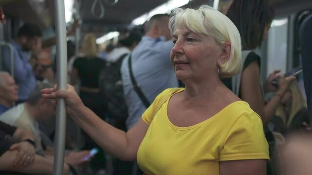 Portrait of smiling senior lady standing in bus, metro train or tram. Group of diverse people passengers in blurred background. High quality FullHD footage