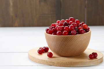 Fresh ripe cranberries in bowl on white wooden table, closeup. Space for text