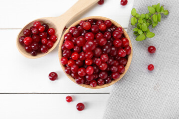 Fresh ripe cranberries and branches on white wooden table, top view