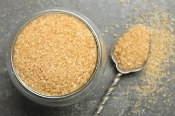 Brown sugar in bowl and spoon on grey textured table, top view