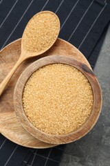 Brown sugar in bowl and spoon on grey table, top view