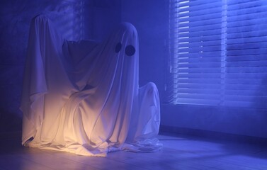 Creepy ghost. Woman covered with sheet near window in blue light