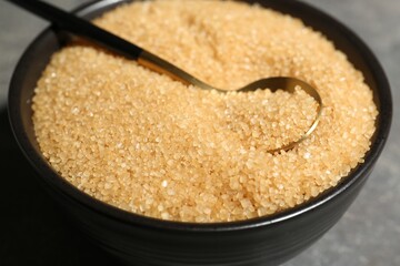 Brown sugar in bowl and spoon on grey table, closeup