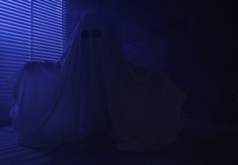 Naklejka premium Creepy ghost. Woman covered with sheet near window in blue light