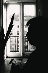 Black and white silhouette of a young man in a vintage room and a cityscaple view on a background - 718219490