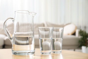 Jug and glasses with clear water on table indoors, closeup. Space for text