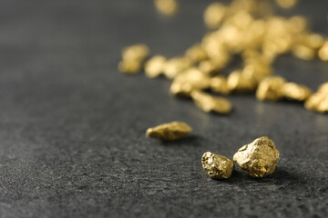 Shiny gold nuggets on grey textured surface, closeup. Space for text