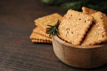 Cereal crackers with flax, sesame seeds and rosemary in bowl on wooden table, closeup. Space for text