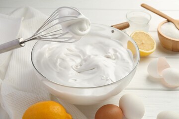 Bowl with whipped cream, whisk and ingredients on white wooden table