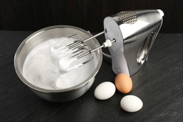 Bowl with whipped cream, hand mixer and eggs on black table