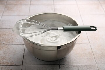 Bowl and whisk with whipped cream on tiled table