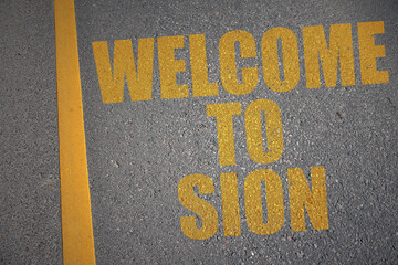 asphalt road with text welcome to Sion near yellow line.