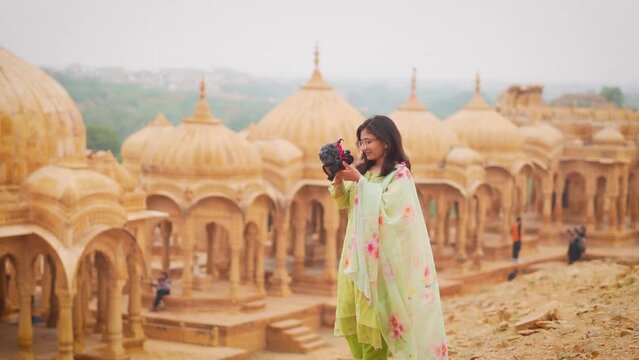 Teenager Indian girl taking photo of sandstone monuments of Bada Bagh at Jaisalmer, Rajasthan, India. Traveler woman in Rajasthan taking photo using DSLR camera. Photographer working.