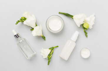 Facial cosmetic products with freesia flowers on color background, top view