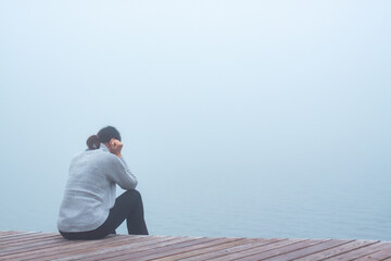Junge Frau sitzt einsam am Rand eines Holzweges einer Brücke gebückt und traurig in Gedanken...
