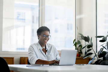 African black businesswoman using laptop at office. Smiling midlle-aged female office employee looking at the laptop screen, Successful woman entrepreneur.