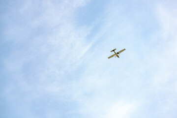 Single engine ultralight plane flying in the blue sky with white clouds. Small private plane flying in light white clouds, bottom view. Light aircraft in the sky with clouds, minimalistic style photo