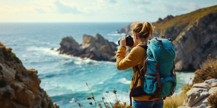 A woman with a backpack capturing a scenic view of the ocean. Suitable for travel and adventure themes