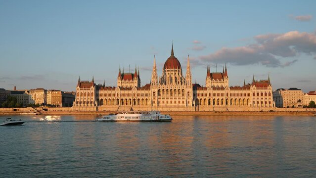 Residence of Hungarian Parliament, Budapest timelapse against backdrop of sunset on sunny day in summer. National symbol view from other bank of Danube Rive. Floating river pleasure passenger vessels