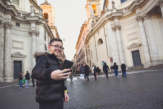 Smiling Happy tourist  boy with   eyeglasses  enjoy the city of Rome  and making photos with a phone during language vacation.Concept  family travel trip happy language vacations in Rome