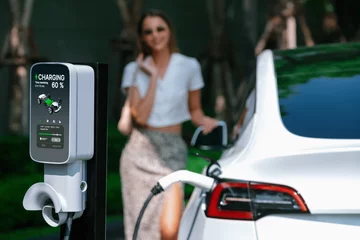 Fotobehang Young woman travel with EV electric car charging in green sustainable city outdoor garden in summer. Urban sustainability lifestyle by green clean rechargeable energy of electric BEV vehicle innards © Summit Art Creations