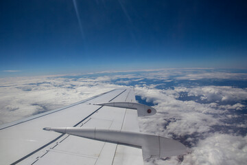 Aerial view by the airplane wing while flying above the clouds with a blue sky in the background, wide angle shot