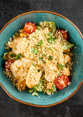 Top view of a quinoa salad with grilled chicken, cherry tomatoes, and mixed greens, served in a turquoise ceramic bowl