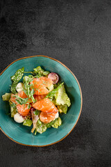 Top-down view of a fresh salad with salmon, mozzarella, avocado, and mixed greens in a turquoise bowl