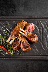Juicy grilled lamb rack with a crusty sear, accented by fresh green herbs and a fiery red chili on...