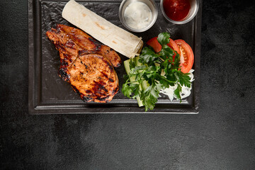 Juicy grilled pork loin served with a side of fresh vegetables, lavash bread, and a selection of...