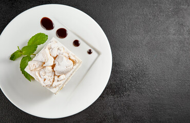 Delicate meringue cake with creamy cheese filling, garnished with a sprig of mint on a white plate