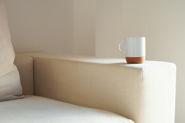 Fototapeta na wymiar A white mug with a cork bottom on white sofa in the morning light