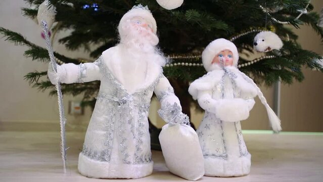 toy of Santa Claus and Snow Maiden are standing near christmas tree.