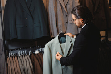 Portrait business gentleman in glasses chooses to buy suit jacket in shop store classic clothes for...