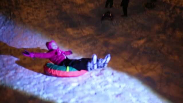 Happy girl rides on snowtube in ray of light in winter evening