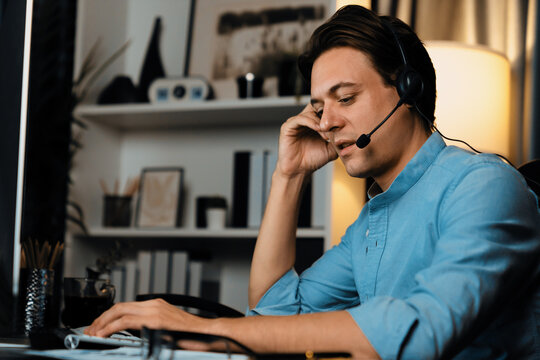 Call center consulting with customers on headphones on monitor in business paragraph with typing on pc with dynamic data marketing analysis planning at modern home office at night time. Pecuniary.