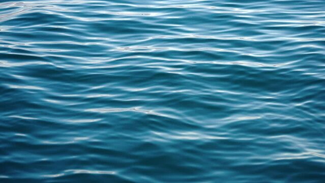 Blue texture water surface small waves slow motion move form ripples at sunset in summer evening. Nature. Motion of small waves. Sea idyll. Relax