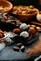 Four handmade chocolate candies on spatula on blackstone stand in heart shape. Closeup chocolate candies with cocoa beans, nuts around