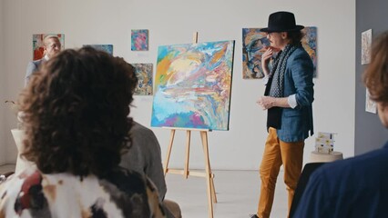Medium full zoom shot of eccentric young Caucasian male artist demonstrating new artwork to diverse public and press in art gallery, describing his inspiration and creative process, cameras flashing