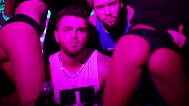Two guys singing microphone and gesticulating among sexy girls dancing