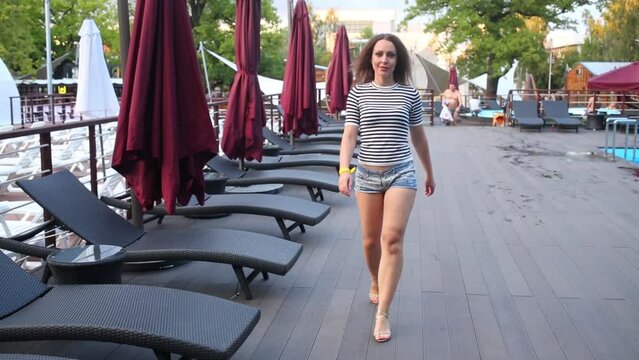 Young woman in striped T-shirt is walking near pool.