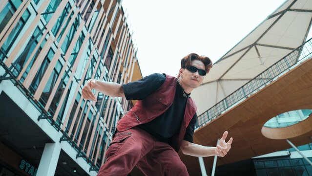 Low angle of asian attractive hipster pose at camera surround by mall. Portrait of break dance choreographer looking at camera while dancing in hip hop style. Outdoor sport 2024. Endeavor.